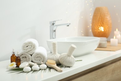 Spa composition. Rolled towels, herbal bags, cosmetic products and burning candles on white countertop in bathroom