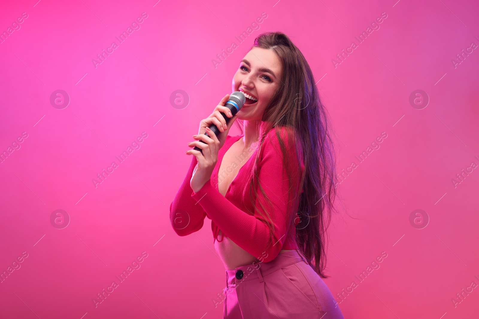 Photo of Emotional woman with microphone singing on pink background. Space for text