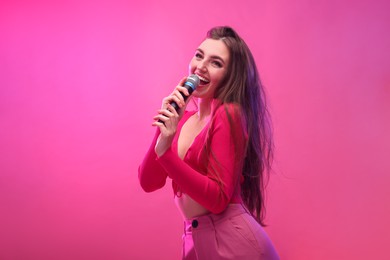 Photo of Emotional woman with microphone singing on pink background. Space for text