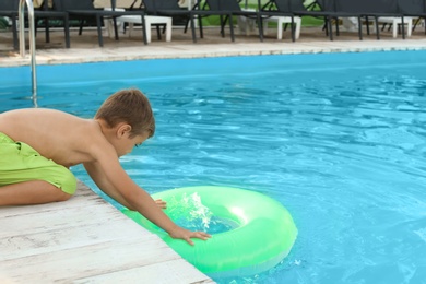 Photo of Little child reaching for inflatable ring in outdoor swimming pool. Dangerous situation