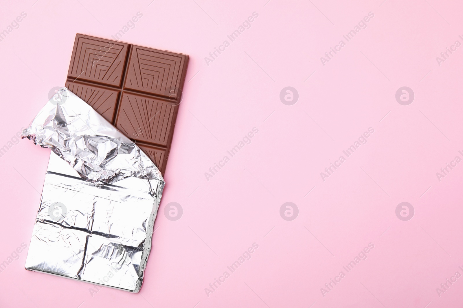 Photo of Tasty chocolate bar on pink background, top view. Space for text