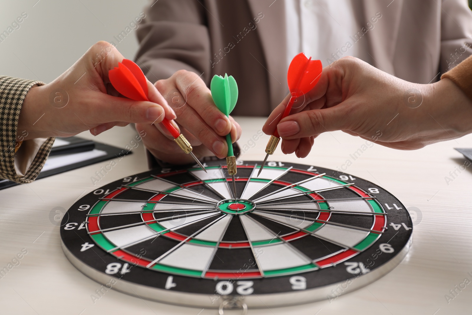 Photo of Business targeting concept. People with darts aiming at dartboard at table, closeup