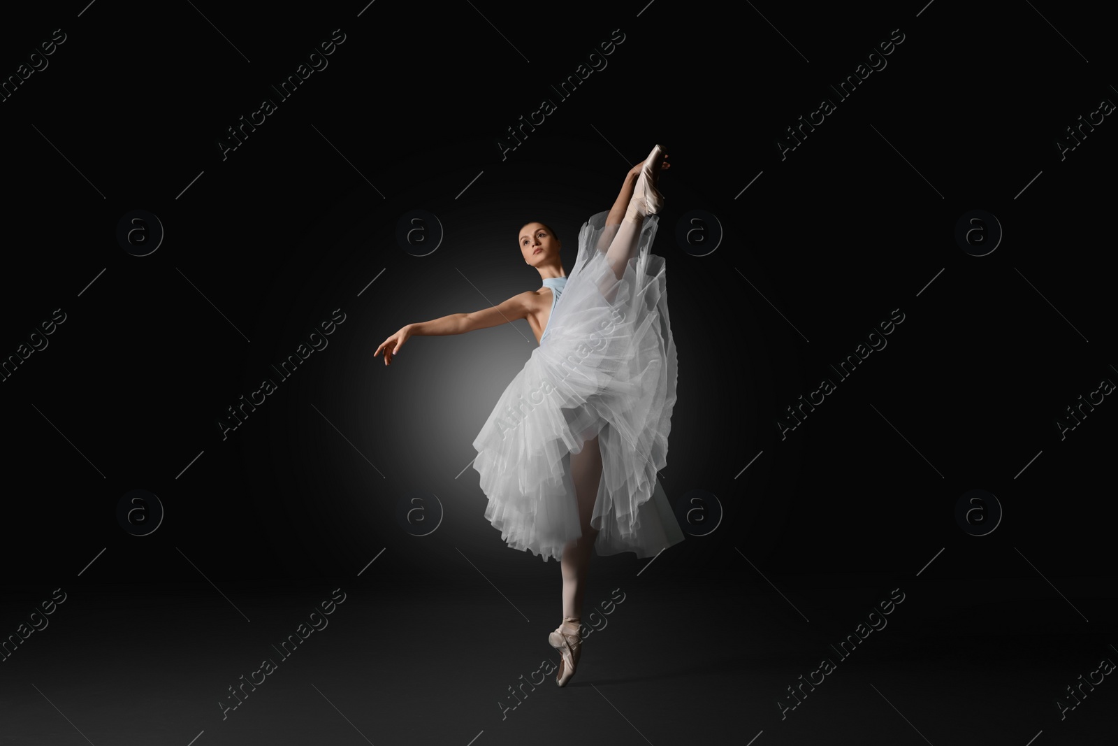 Photo of Young ballerina practicing dance moves on black background