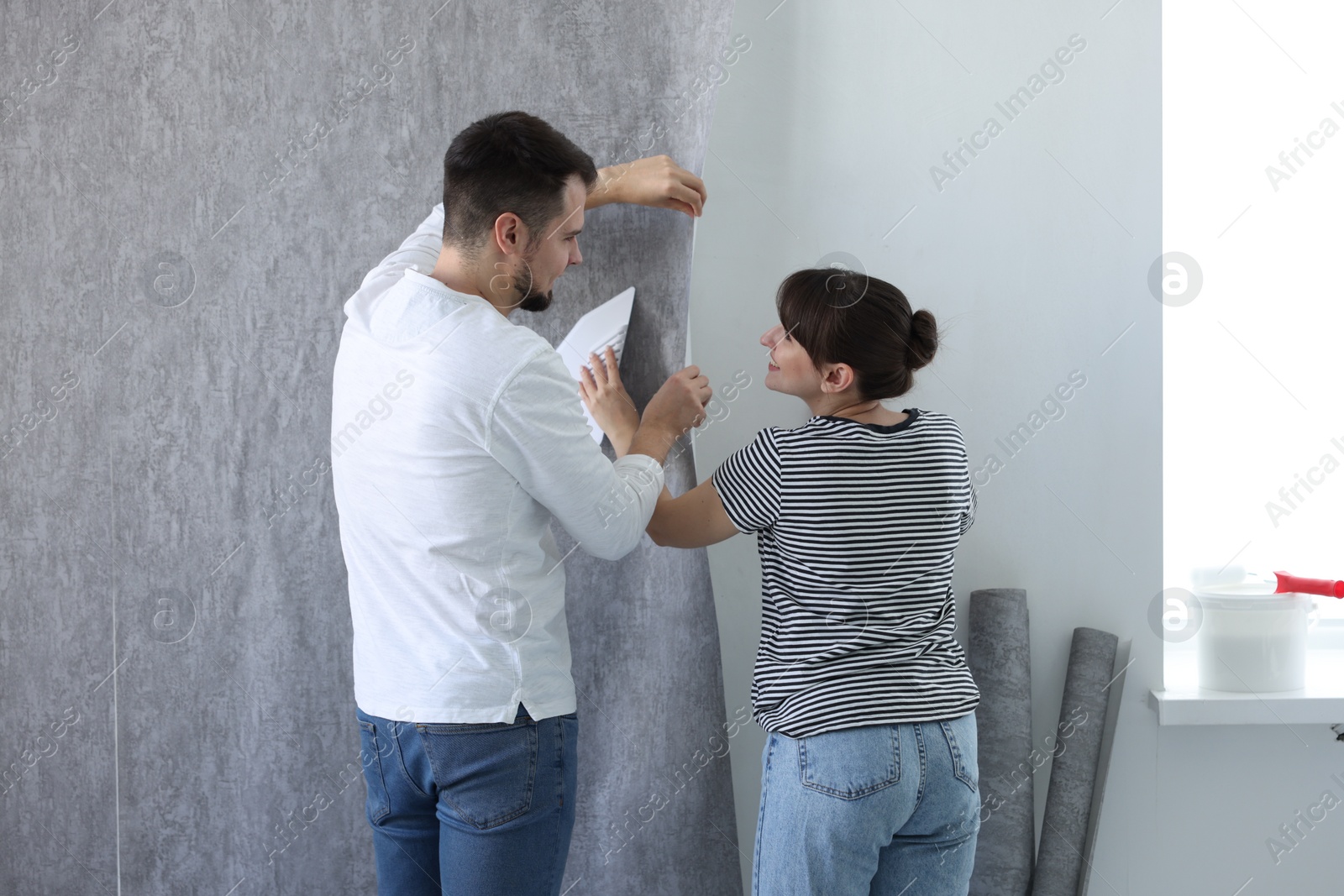 Photo of Woman and man hanging gray wallpaper in room, back view