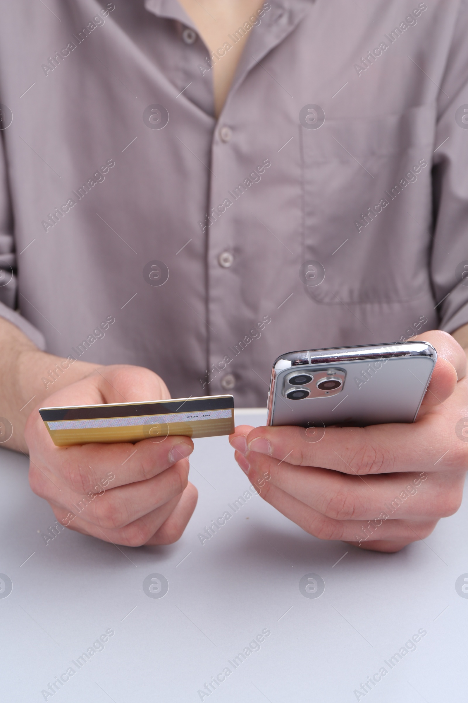 Photo of Online payment. Man with smartphone and credit card at light grey table, closeup