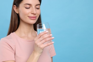 Photo of Healthy habit. Woman holding glass with fresh water on light blue background. Space for text