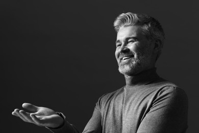 Photo of Portrait of smiling man gesturing on dark background. Black and white effect