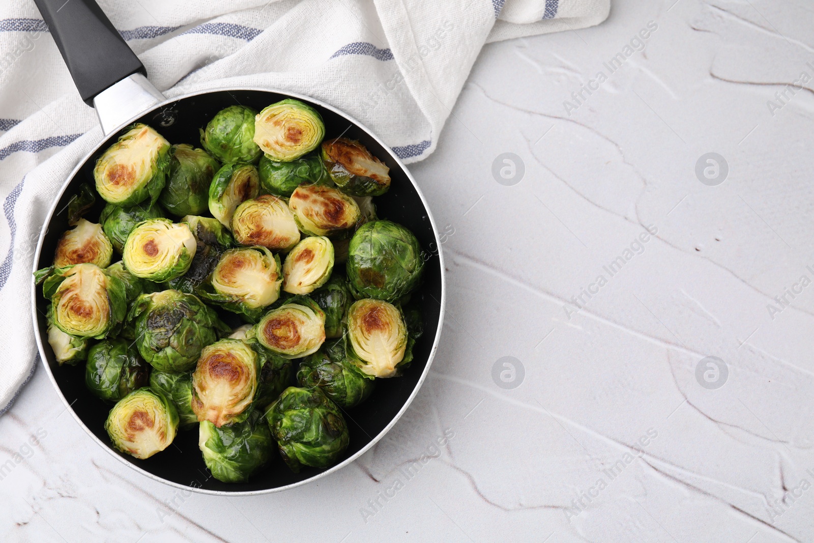 Photo of Delicious roasted Brussels sprouts in frying pan on white textured table, top view. Space for text