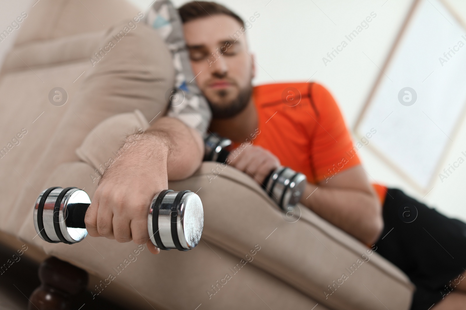 Photo of Lazy young man with sport equipment on sofa at home, focus on hand