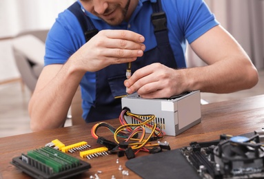 Photo of Male technician repairing power supply unit at table indoors, closeup