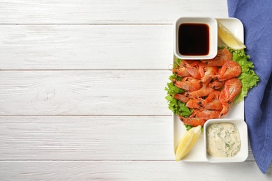 Plate with juicy shrimps and sauces on table, top view