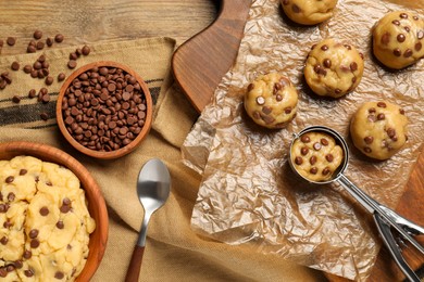 Photo of Bowl with dough and uncooked chocolate chip cookies on wooden table, flat lay