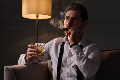 Photo of Handsome man with glasswhiskey smoking cigar at home