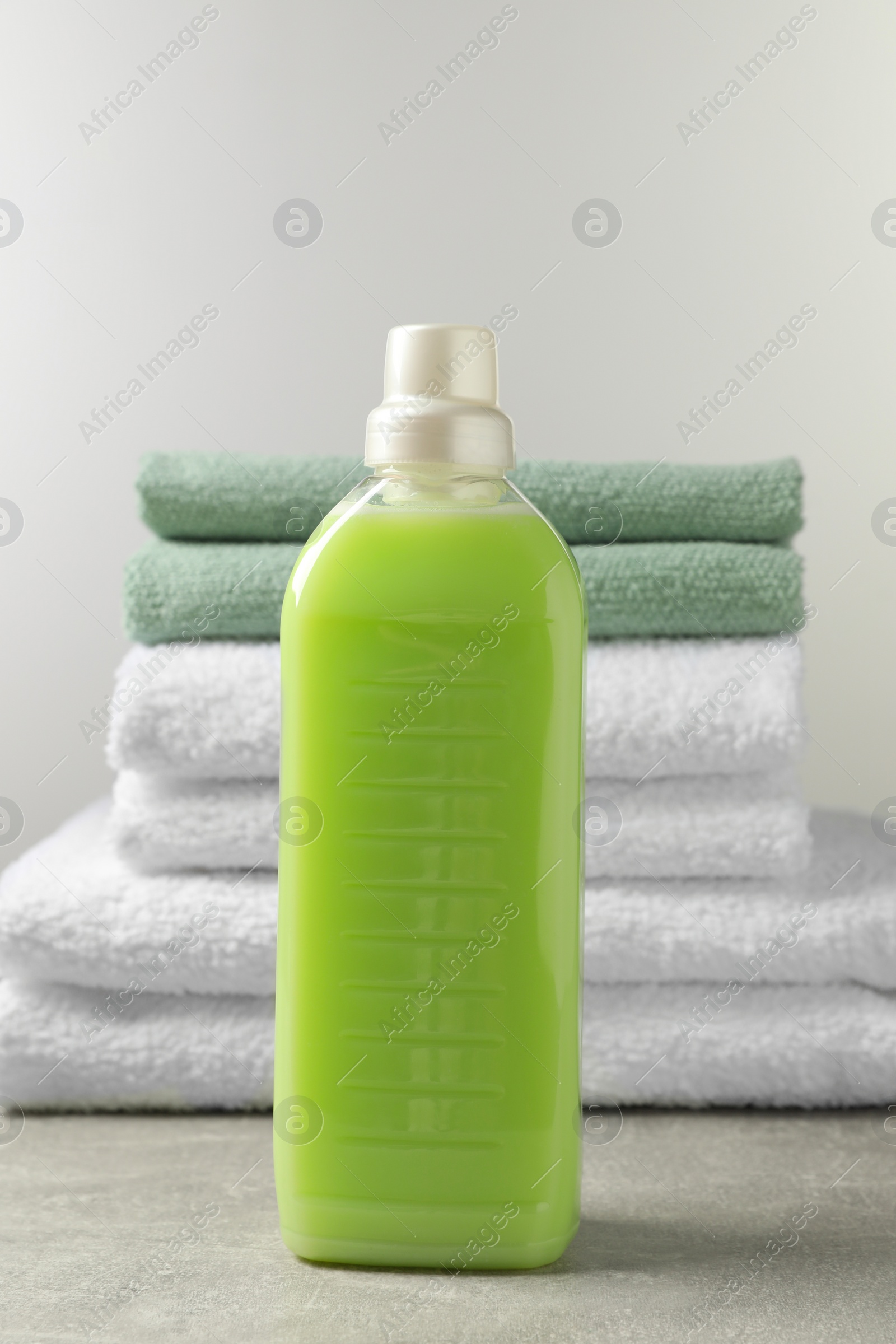 Photo of Bottle of laundry detergent and stacked fresh towels on grey table