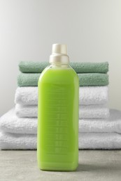 Bottle of laundry detergent and stacked fresh towels on grey table
