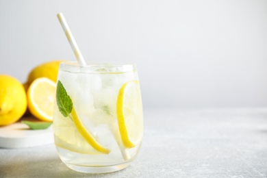Photo of Glass of cold lemonade on light grey table, closeup. Space for text