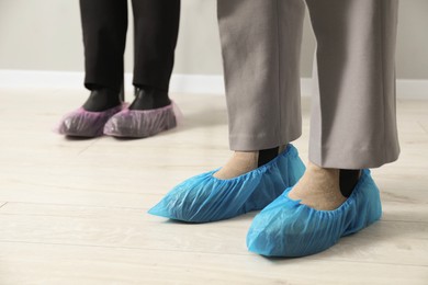Photo of Women wearing blue shoe covers onto different footwear indoors, selective focus