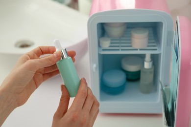 Woman with cosmetic product near mini fridge indoors, closeup