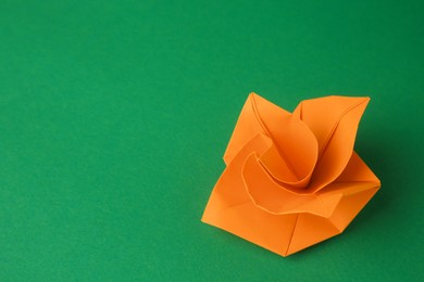 Photo of Origami art. Handmade orange paper flower on green background, space for text