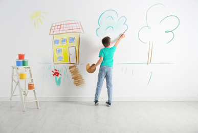 Image of Little child drawing cloud on white wall indoors