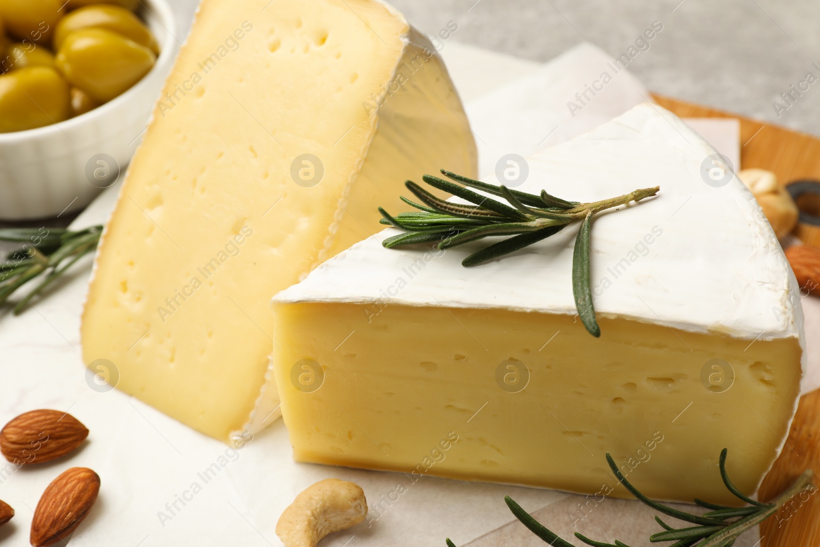 Photo of Pieces of tasty camembert cheese, rosemary and nuts on table, closeup