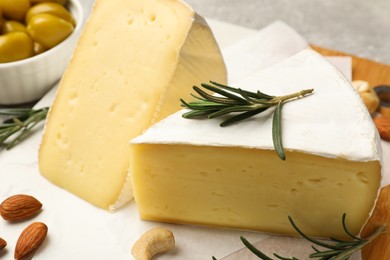 Pieces of tasty camembert cheese, rosemary and nuts on table, closeup