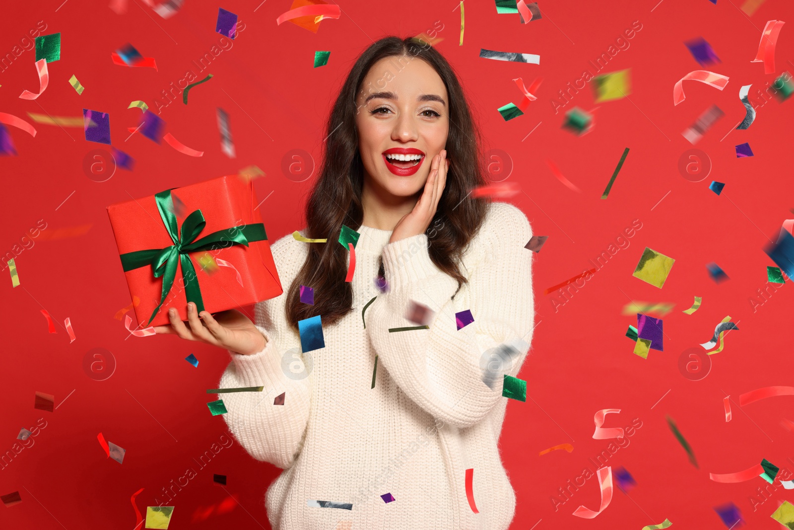 Image of Happy woman with gift box under falling confetti on red background