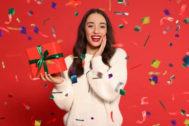 Happy woman with gift box under falling confetti on red background