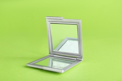 Photo of Stylish cosmetic pocket mirror on light green background