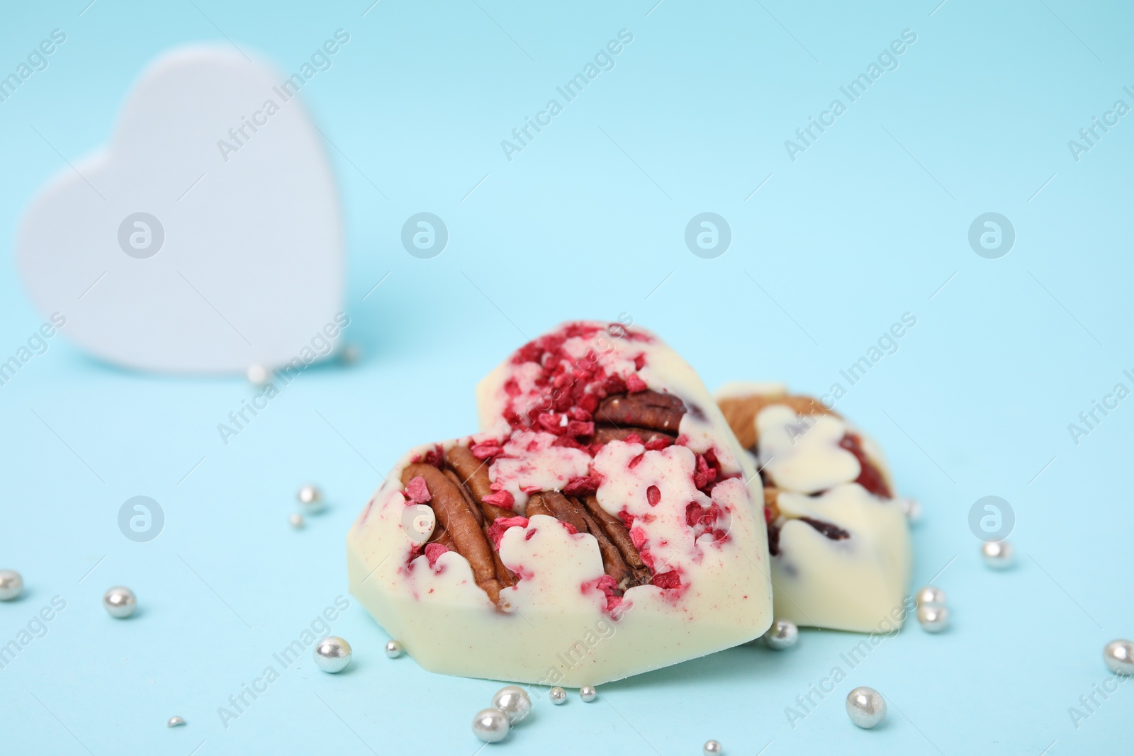 Photo of Tasty chocolate heart shaped candies with nuts on light blue background, space for text