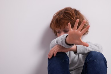 Photo of Child abuse. Boy making stop gesture near grey wall, selective focus. Space for text