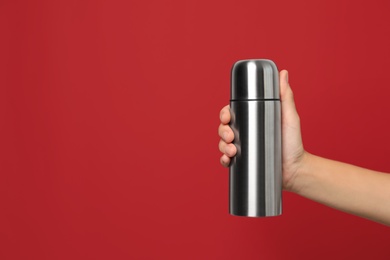 Woman holding modern thermos on red background, closeup. Space for text