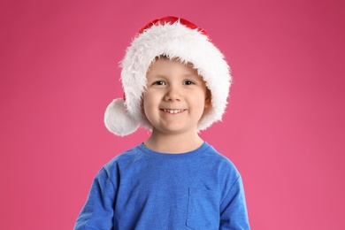 Photo of Cute child in Santa hat on pink background. Christmas celebration