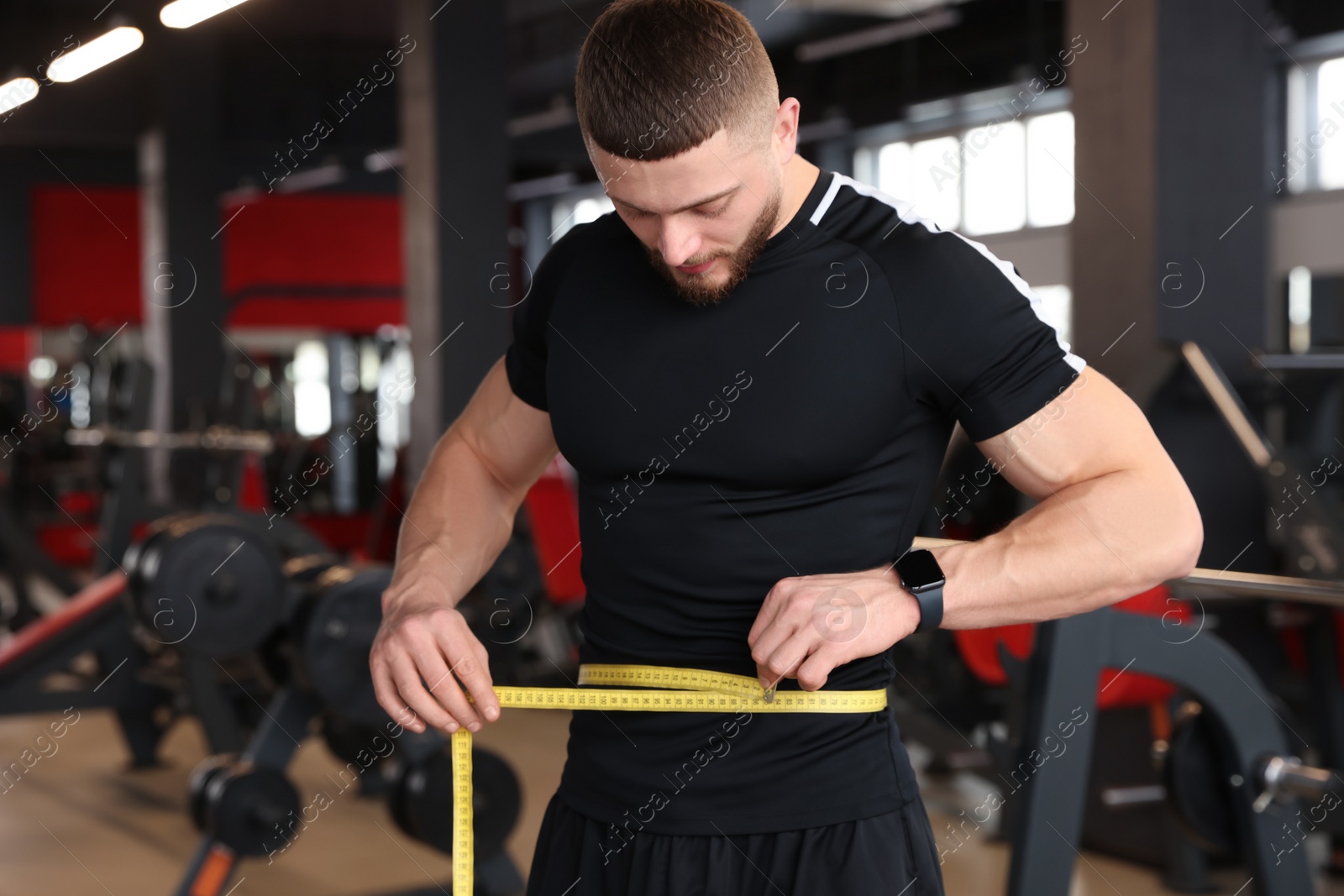 Photo of Athletic man measuring waist with tape in gym