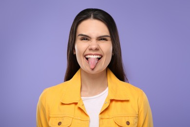 Photo of Happy young woman showing her tongue on purple background