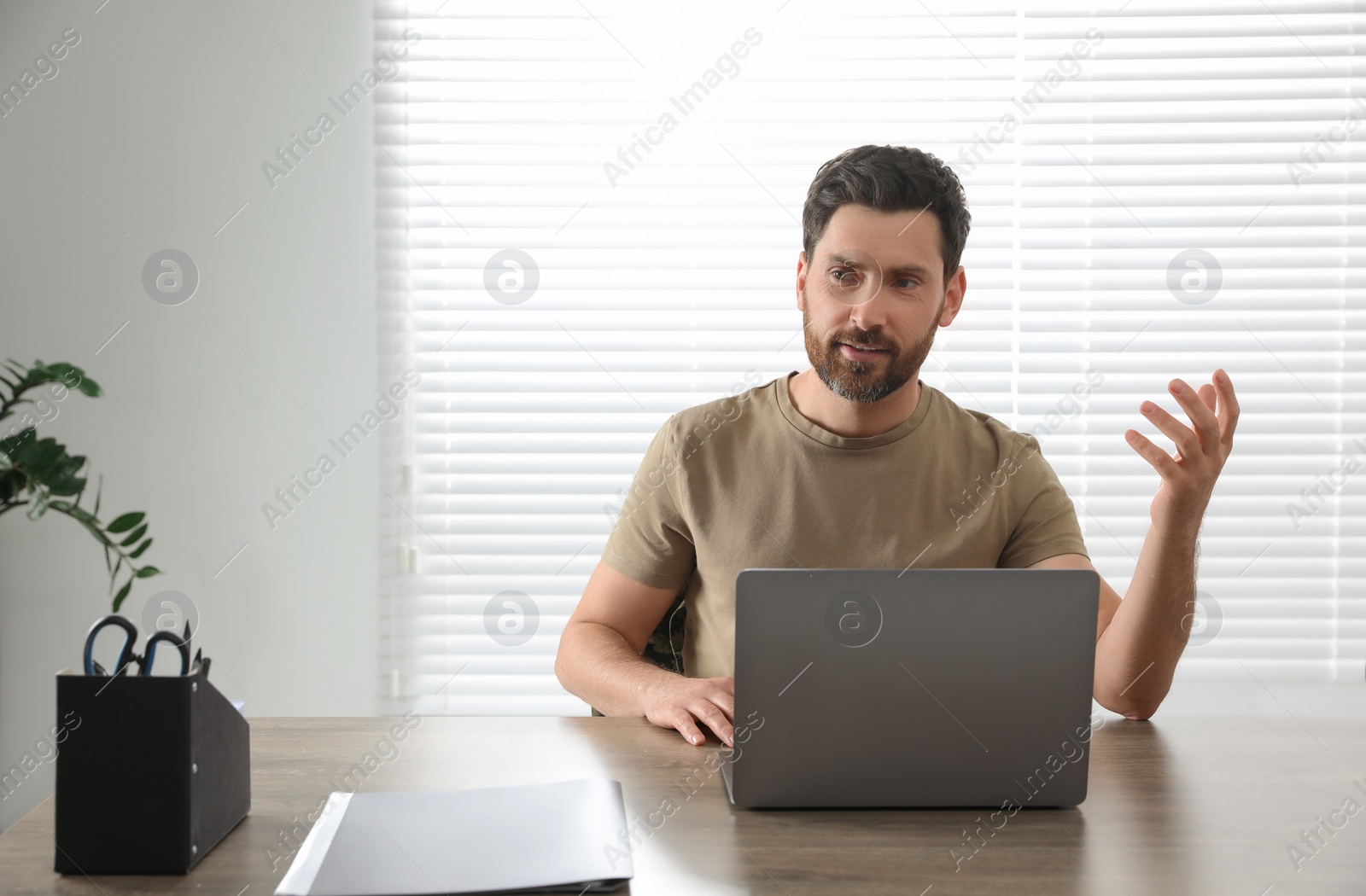 Photo of Soldier using video chat on laptop at wooden table indoors. Military service