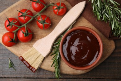 Photo of Marinade in bowl, basting brush, tomatoes and rosemary on wooden table, flat lay