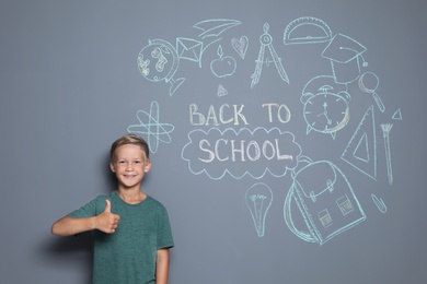 Little child near drawings and text BACK TO SCHOOL on grey background