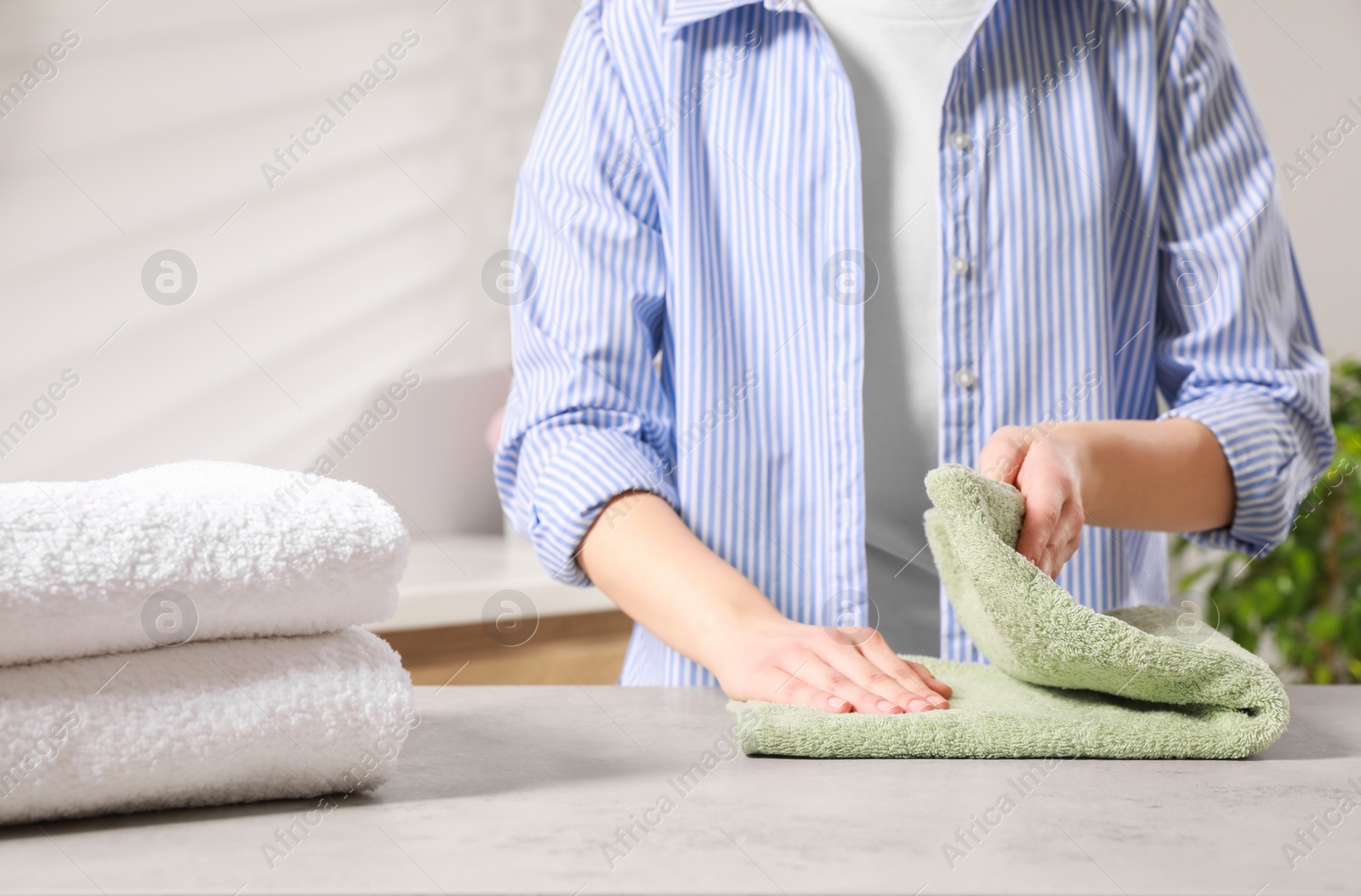 Photo of Woman folding clean terry towel at table indoors, closeup