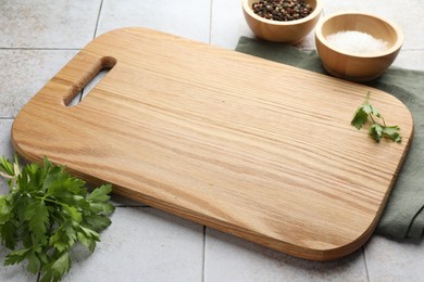 Photo of Cutting board, salt, pepper and parsley on white tiled table. Space for text