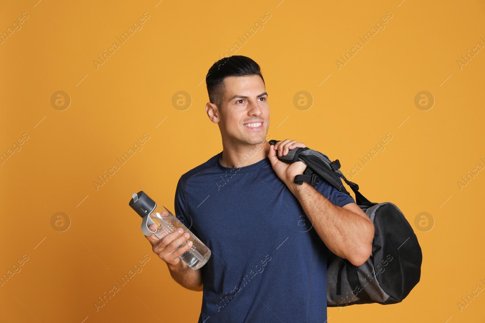 Photo of Handsome man with sports bag and bottle of water on yellow background