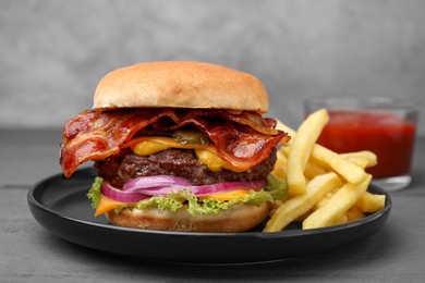 Photo of Tasty burger with bacon, vegetables and patty served with french fries on grey wooden table, closeup