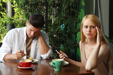Photo of Young woman with smartphone ignoring her boyfriend in outdoor cafe. Boring date