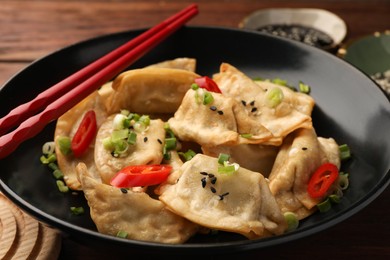 Photo of Delicious gyoza (asian dumplings) with sesame seeds, green onions and chili peppers on table