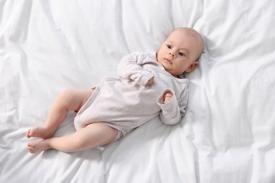 Photo of Cute little baby lying on white sheets, top view