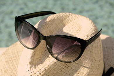 Stylish hat and sunglasses on blurred background, closeup