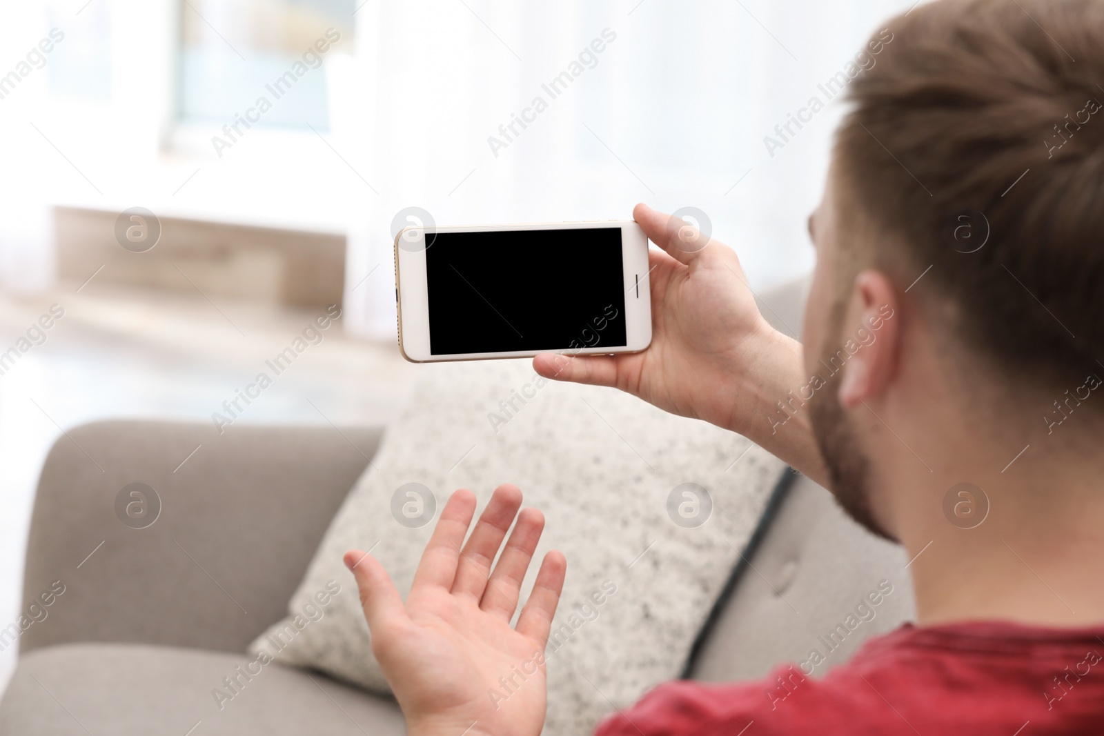 Photo of Young man using video chat on smartphone in living room, closeup. Space for design