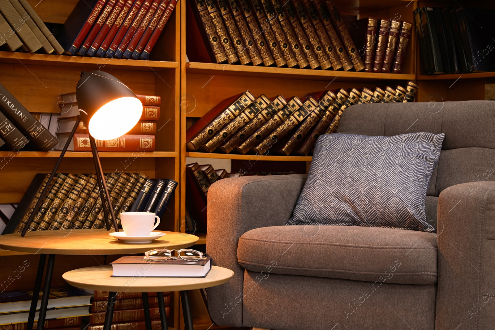 Photo of Book with glasses, table lamp and cup of drink near comfortable armchair in cozy home library