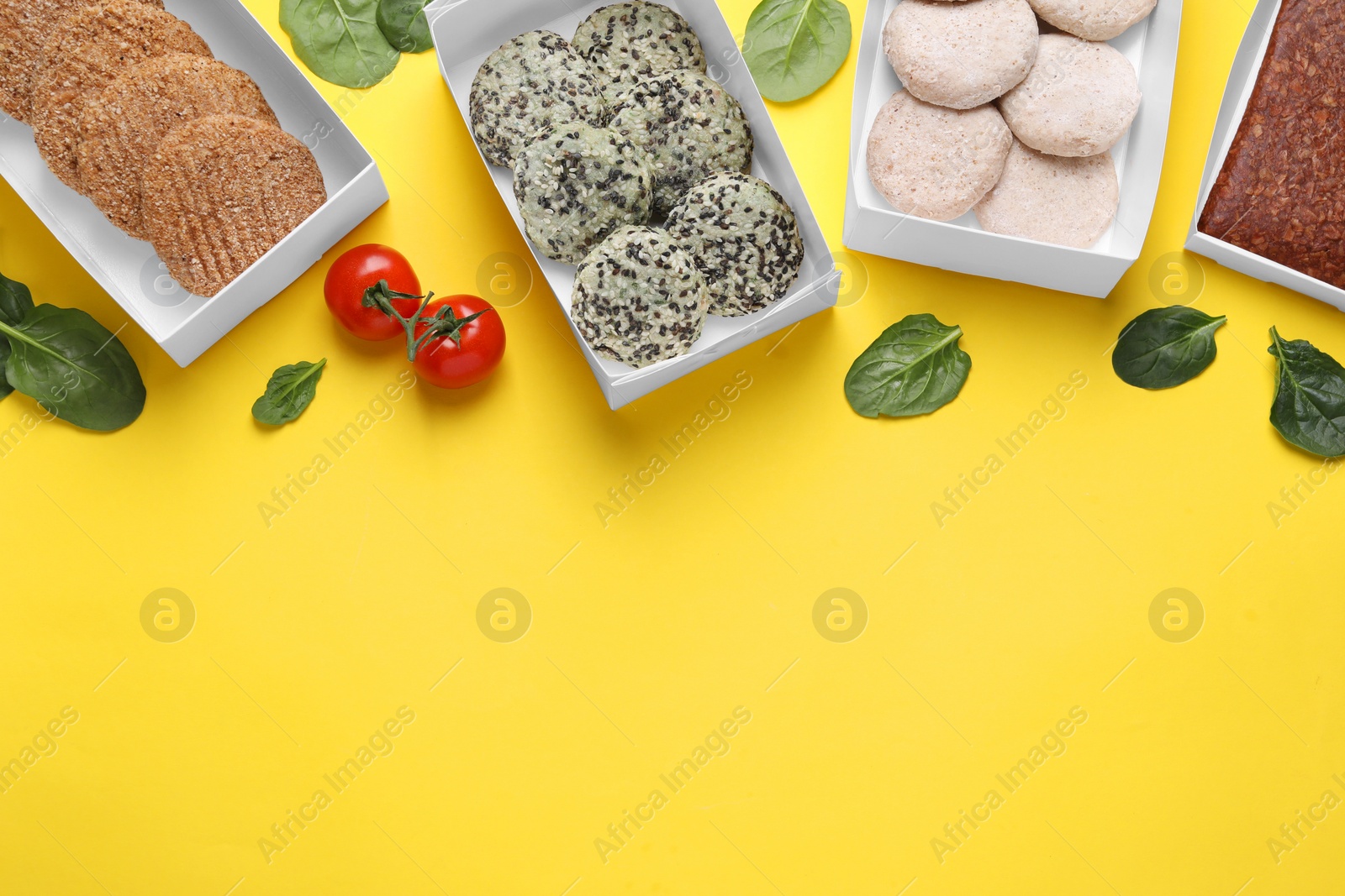 Photo of Many different raw vegan meat products, tomatoes and spinach on yellow background, flat lay. Space for text