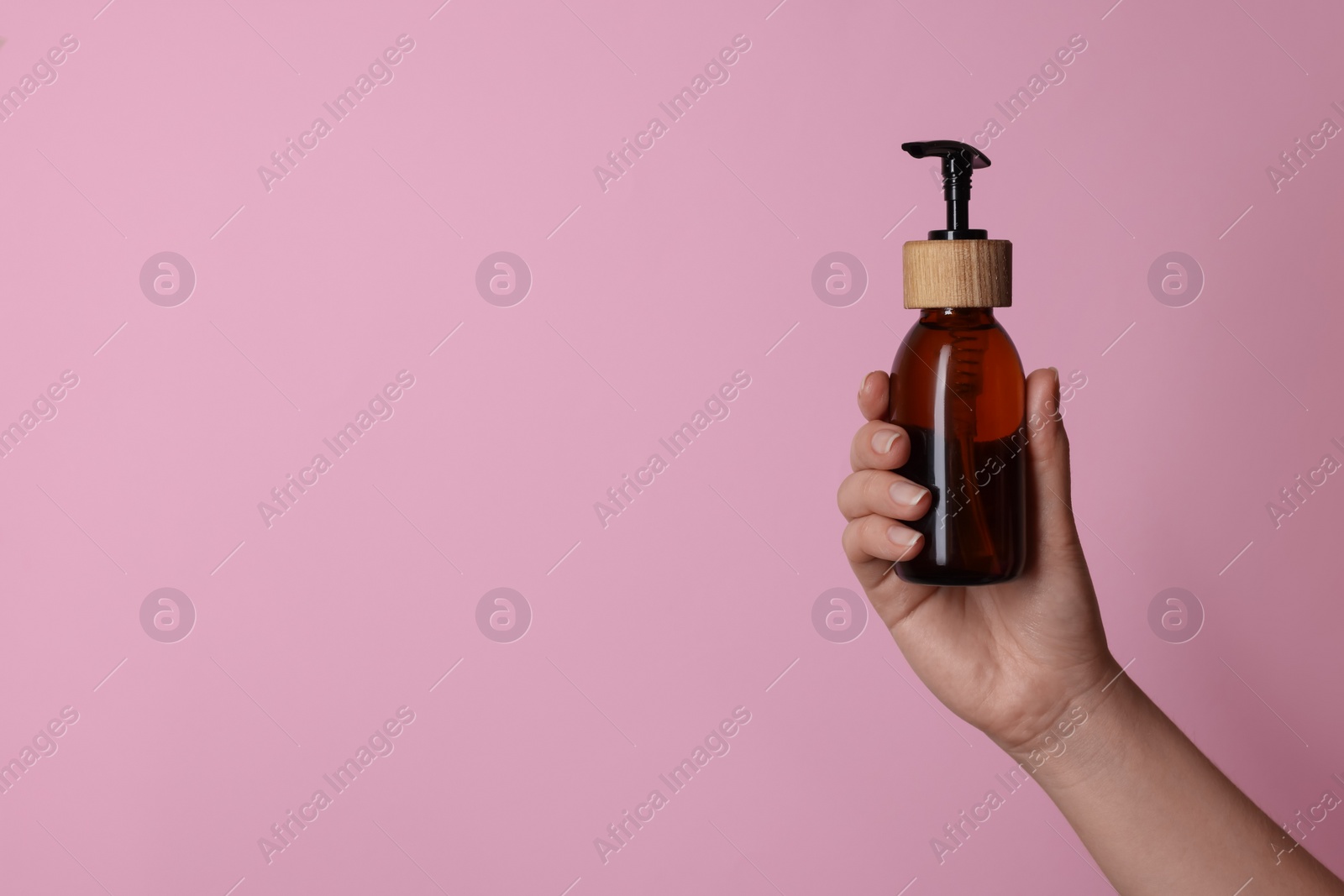 Photo of Woman holding bottle of cosmetic product on pink background, closeup. Space for text